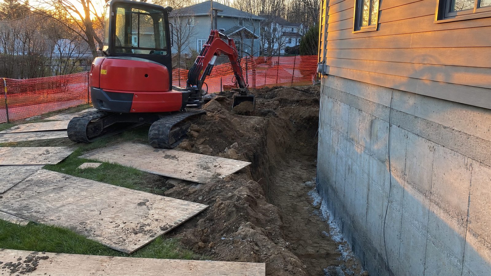 Pelle compacte au bord d&rsquo;une tranchée de fondation en fin de journée